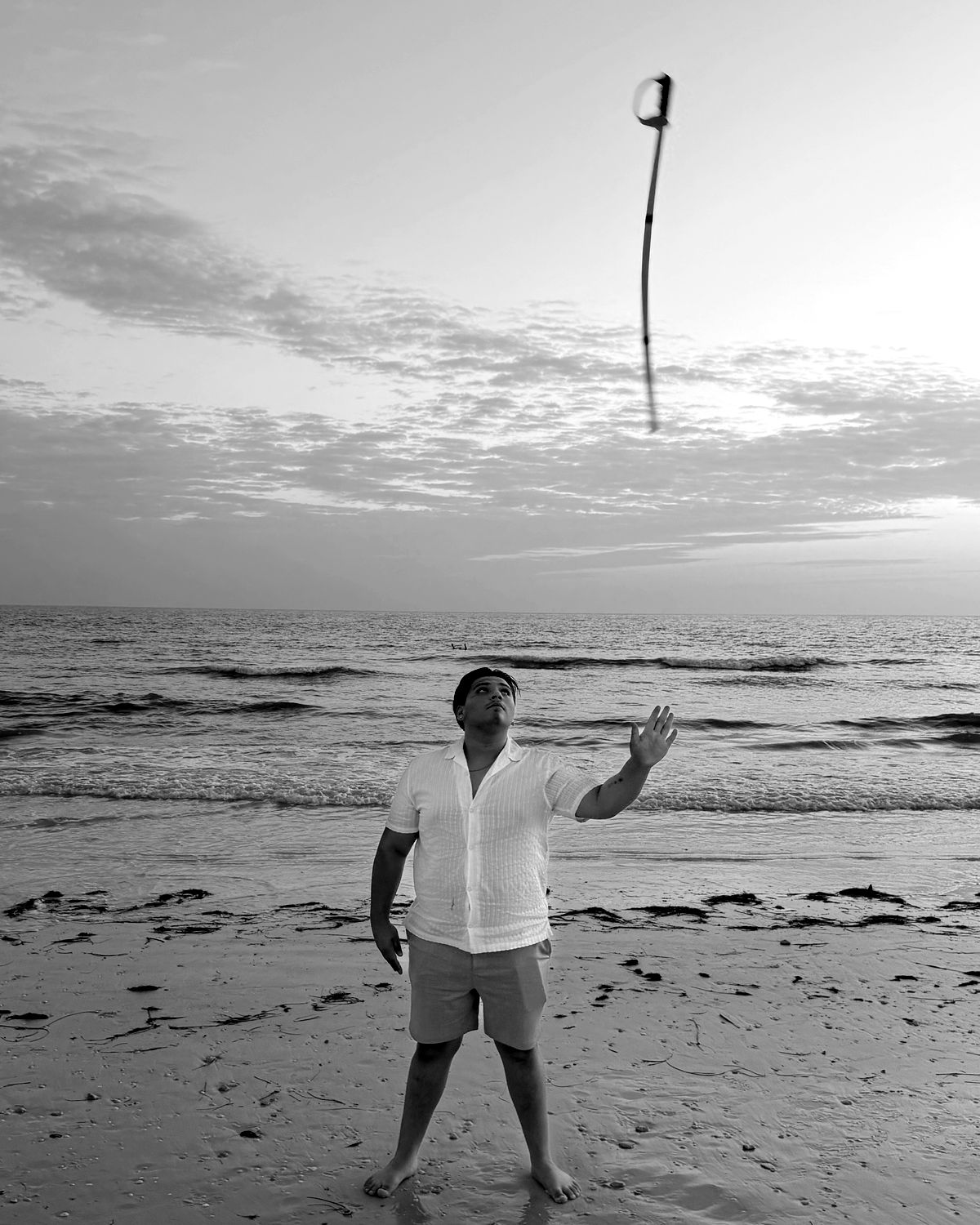 Morgan practicing a rifle toss on the beach at sunset, the rifle high above him.
