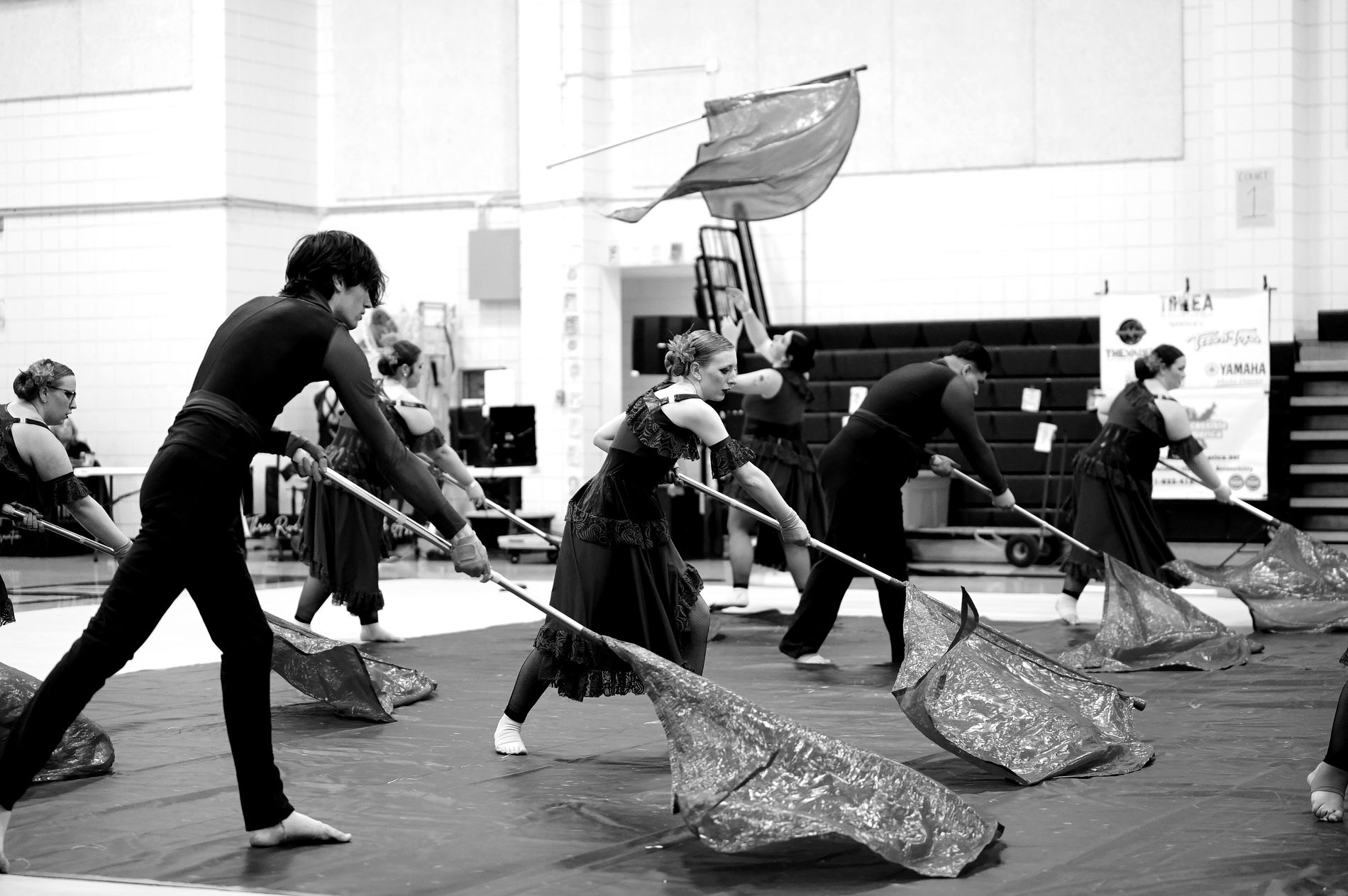 A full color guard line pulling red flags across the floor in performance.